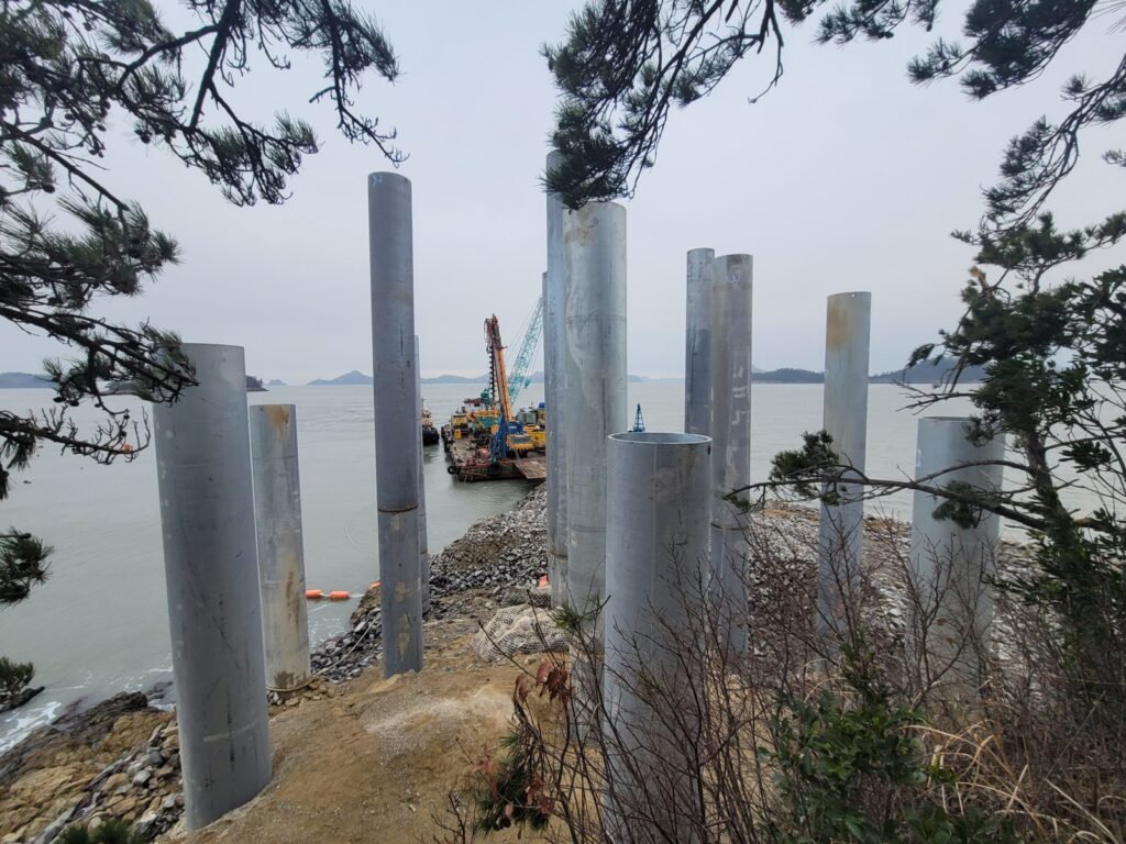 	Completed 1000mm steel pipe piles standing on rock shoreline with work barge in background